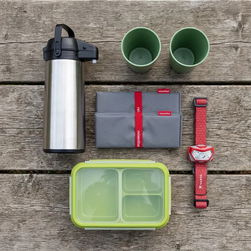 Herbstwanderung mit Zvieri: Thermoskanne, zwei grüne Trinkbecher, gefaltetes Sitzkissen, grüne Lunchbox und rote Stirnlampe auf Holz.
