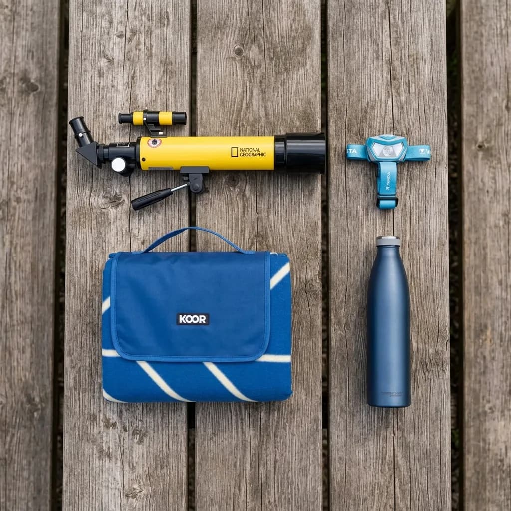 Sterne beobachten: Teleskop, hellblaue Stirnlampe, zusammengefaltete blaue Picknickdecke und dunkelblaue Thermosflasche auf Holzuntergrund.